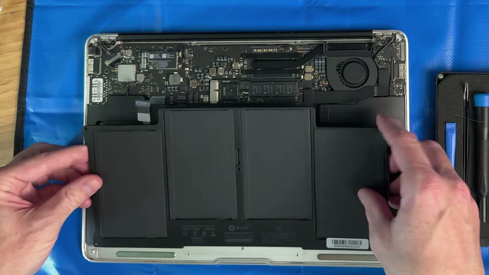 An iFixit replacement battery aligned over the empty battery bay in the 2017 MacBook Air.