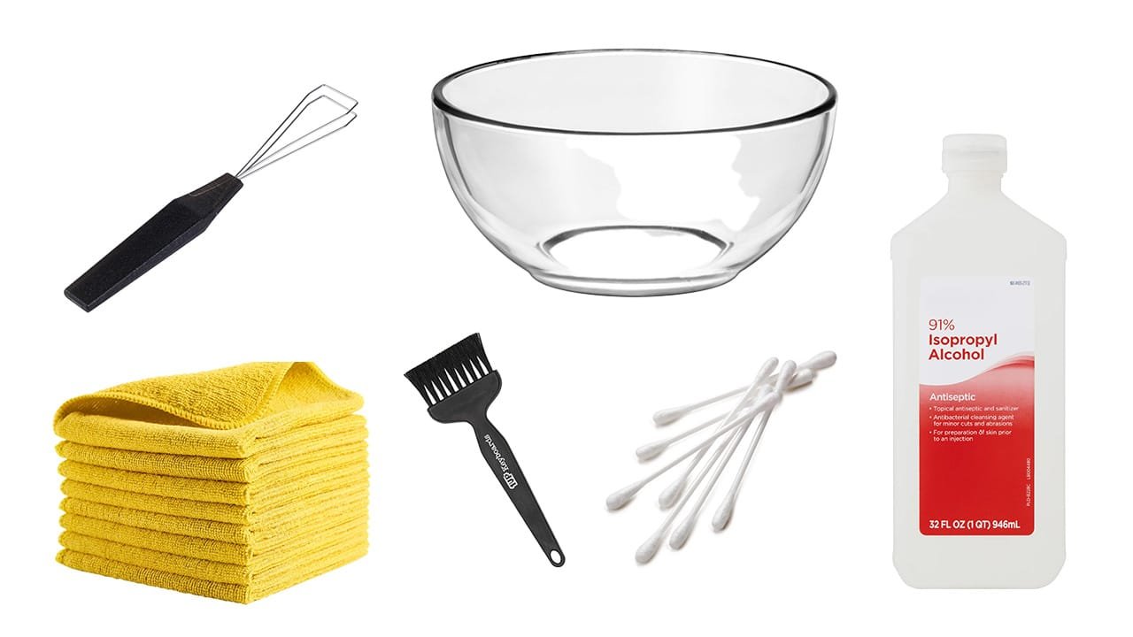 Keyboard cleaning tools laid out including microfiber cloth, brush, cotton swabs, isopropyl alcohol, and keycap puller