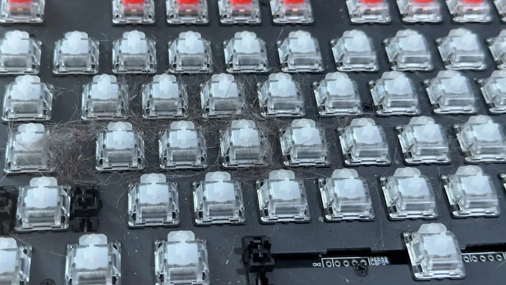Mechanical keyboard with keycaps removed showing dust and debris around switches